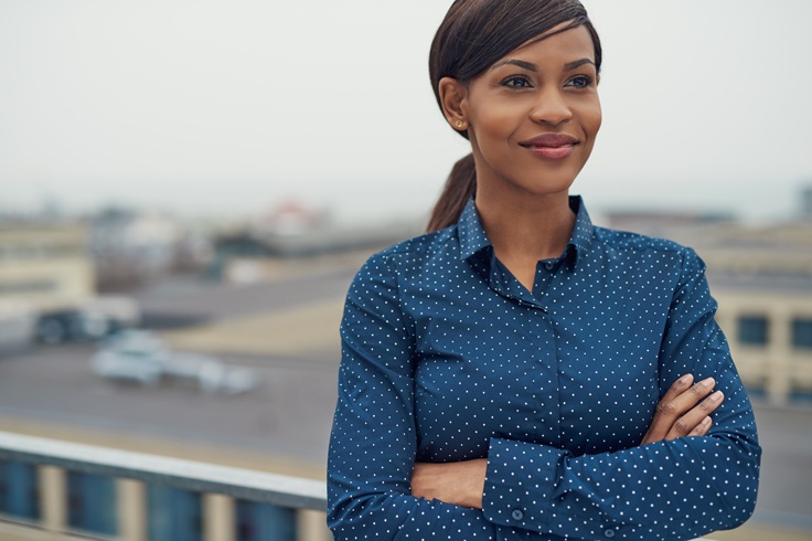 Woman with medium skin tone, smiling and standing confidently with her arms folded.
