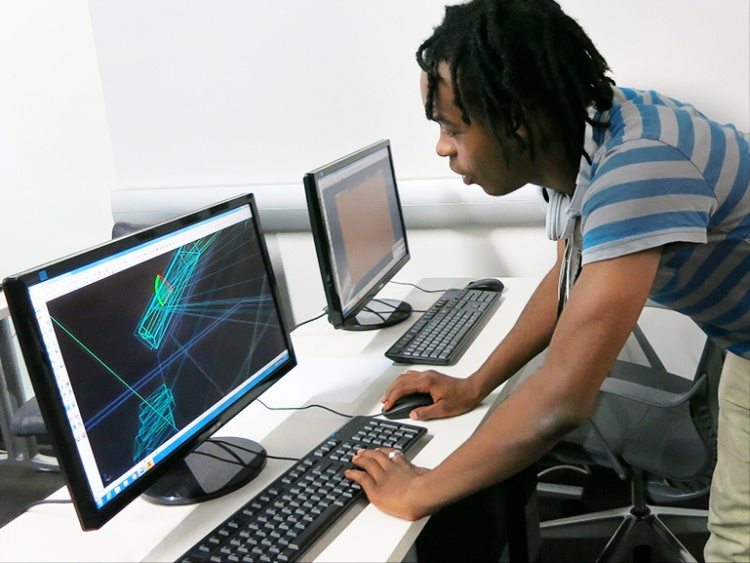Young Black man leaning over a chair and showing spatial imaging at a computer.